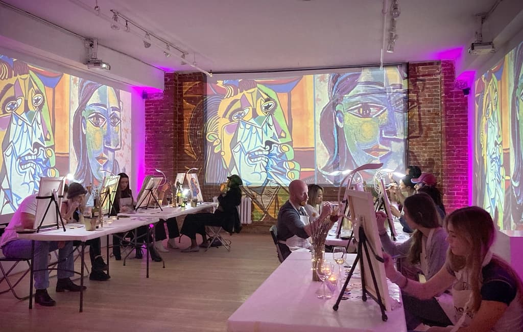 A participant painting a colorful abstract face on canvas with focused attention during a 'Night with Picasso' event.