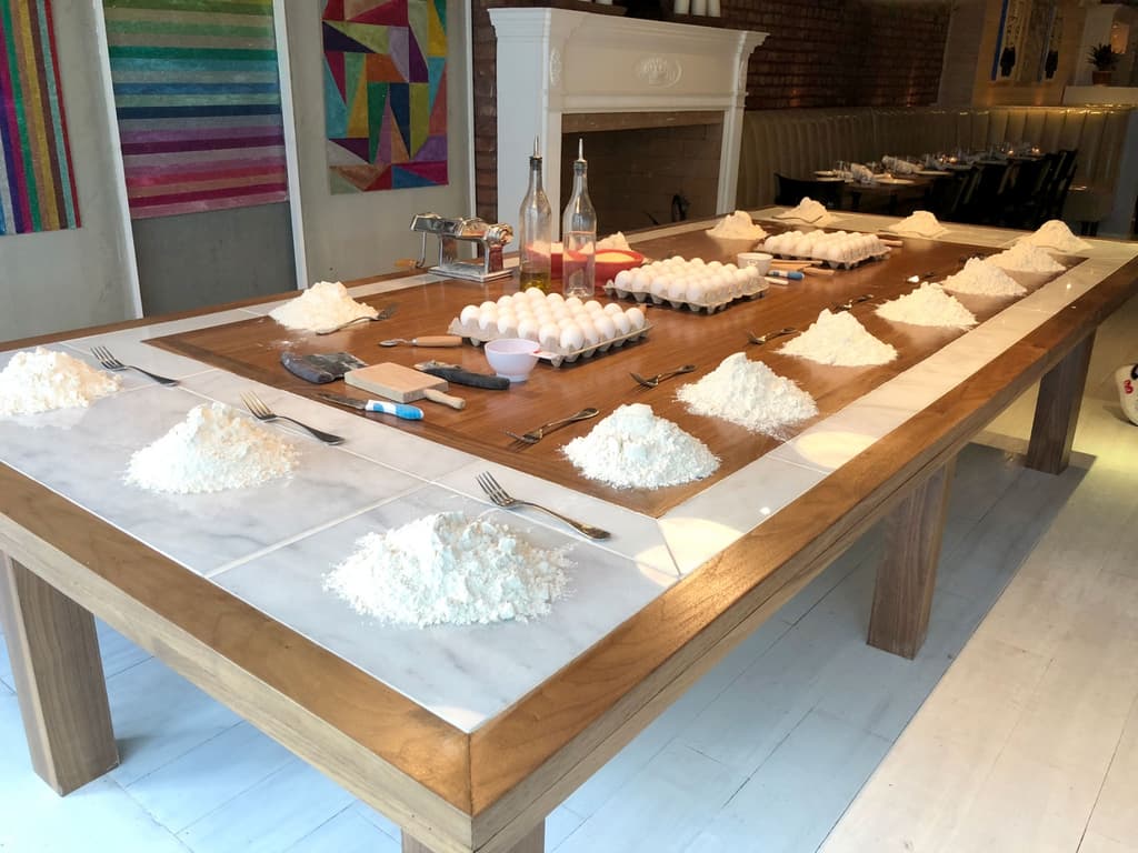 Large table set up for pasta making, with piles of flour and eggs ready for a cooking class or preparation session.