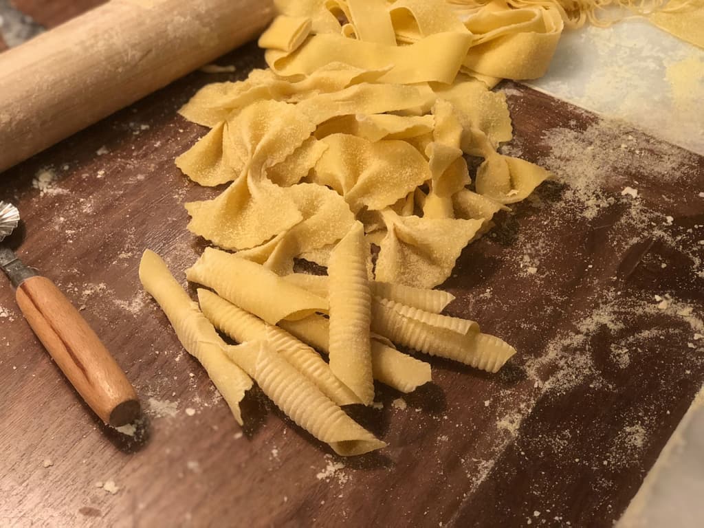 Freshly made pasta on a wooden surface, with a rolling pin and cutter nearby, showcasing homemade preparation.