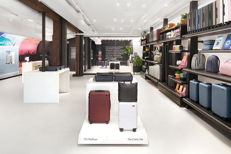 Modern retail space with black Away suitcases on display and travel books on built-in wall shelves.