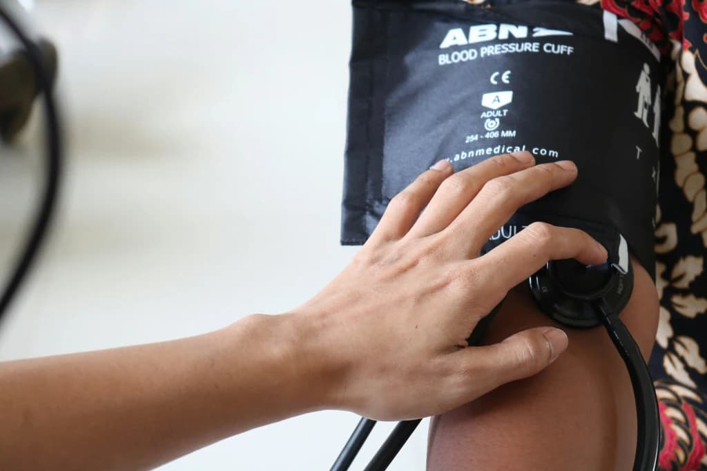 A person checking blood pressure with a stethoscope and an ABN blood pressure cuff on another individual's arm, focusing on health monitoring.