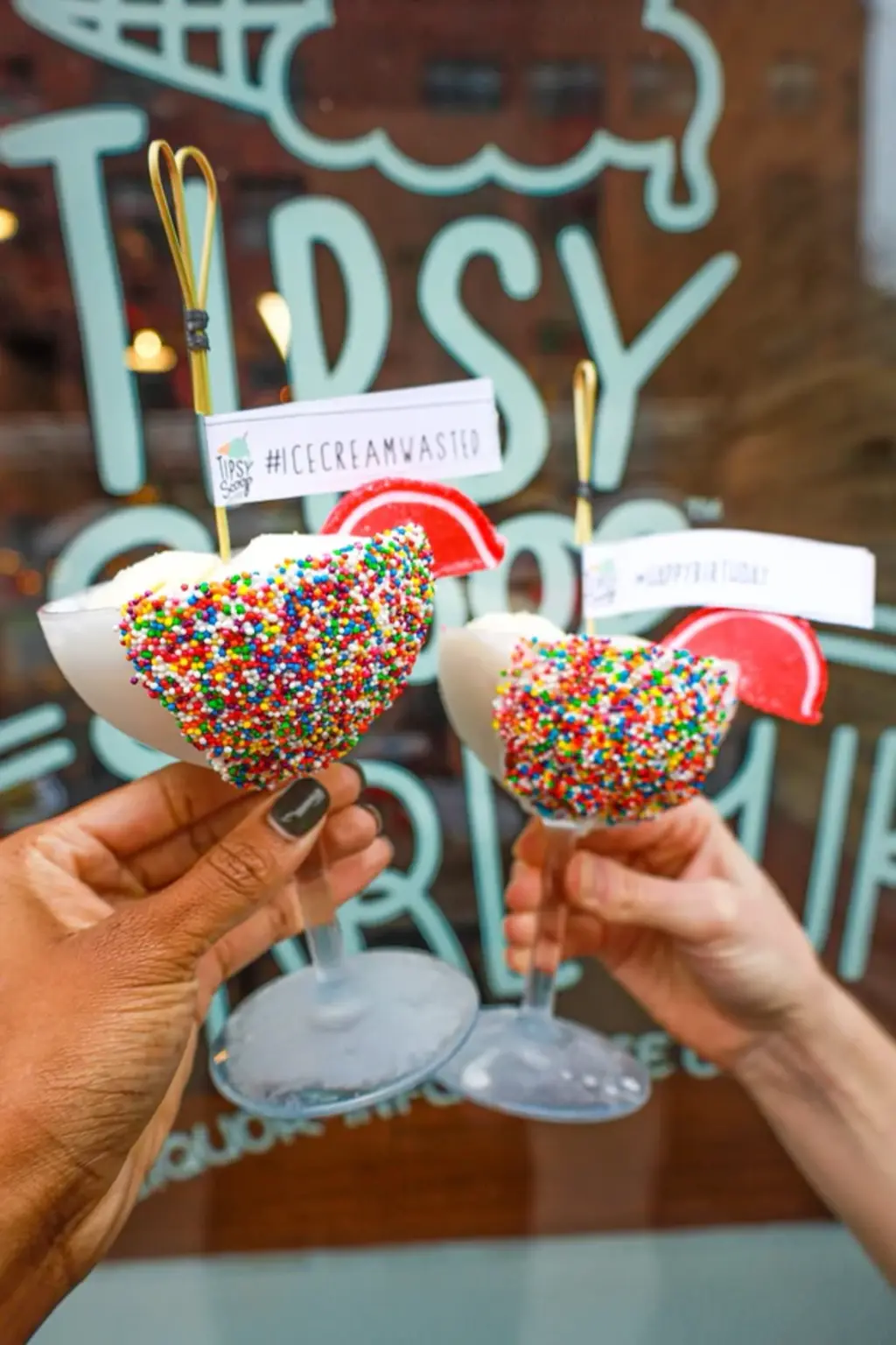 A pint of Santa’s Cookies and Whiskey Ice Cream from Tipsy Scoop, topped with cookies and festive garnishes, next to a stack of chocolate chip cookies.