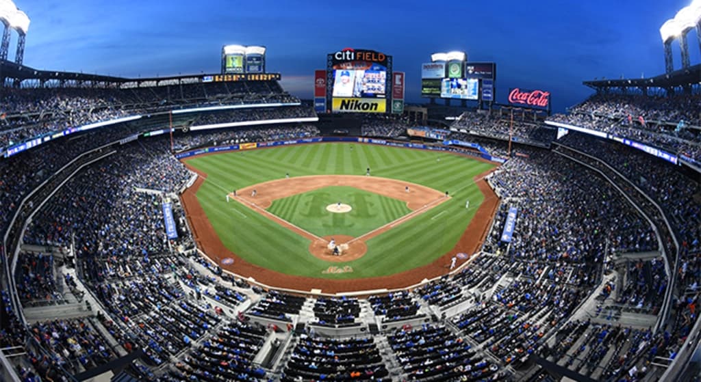 a view of citi field from behind home plate with a game going on and a large crowd in the stands
