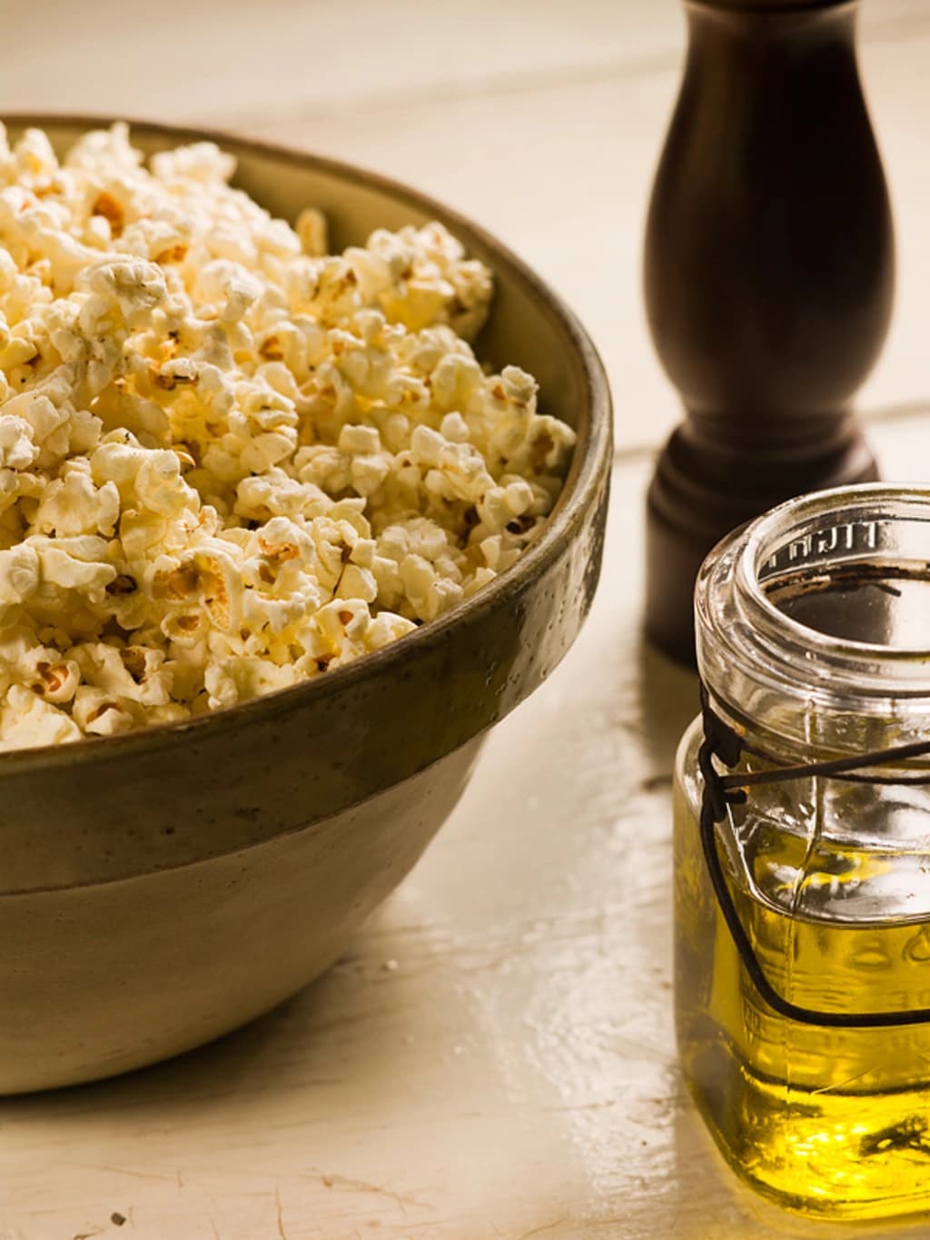 olive oil in a jar next to a bowl of popcorn