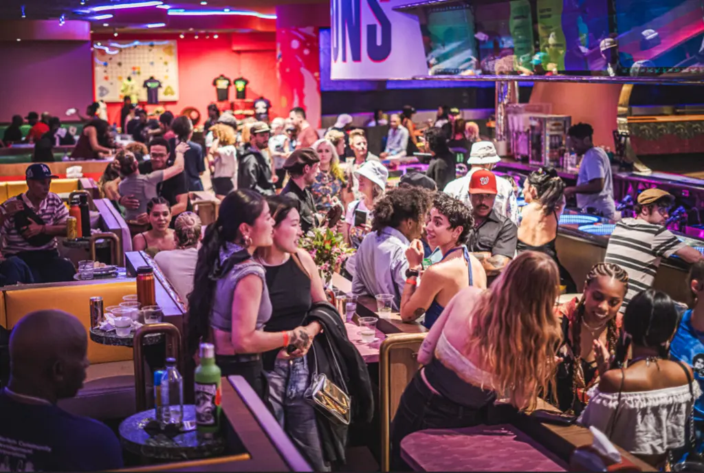 Crowded bar area with people socializing, drinking, and enjoying a lively night out in a colorful, vibrant setting.