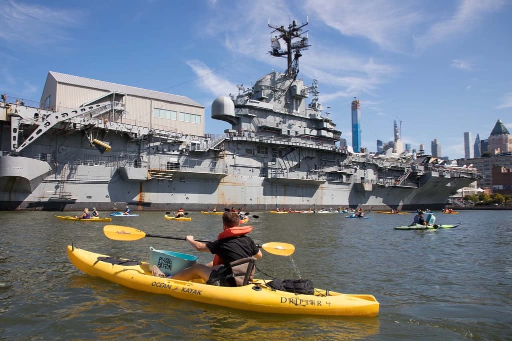 people kayaking around naval ships in the hudson river