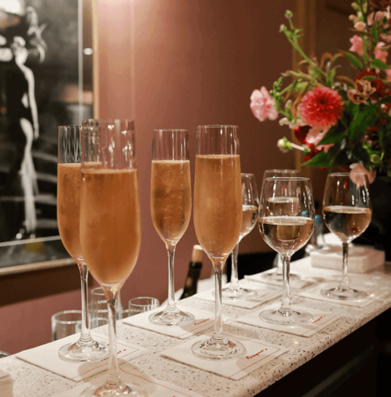 Glasses of sparkling wine and white wine on a bar counter with fresh flowers in the background.